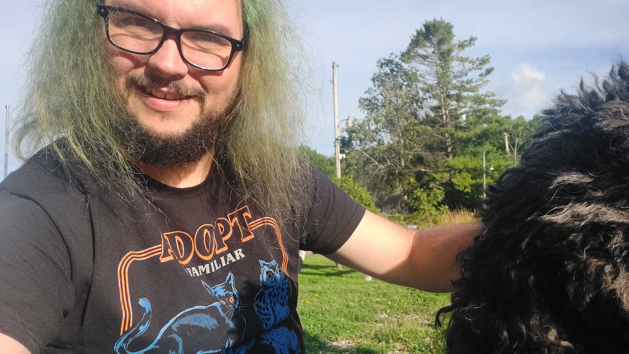 A man with green hair and a beard is outside with a black standard poodle out of frame, Photo 2